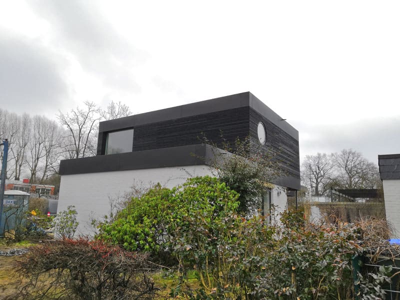 Aufstockung mit dunkler Fassade auf einem weißen Haus